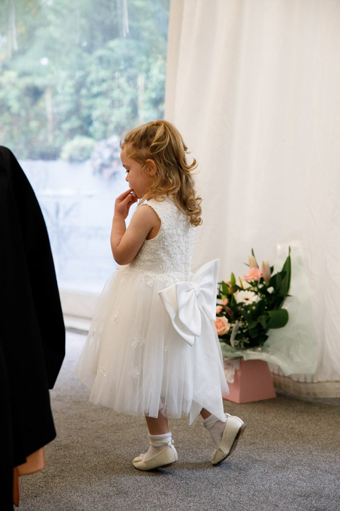 The little bridesmaid walks confidently between tables, exploring the room.