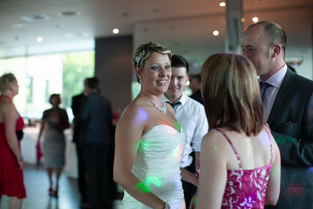 Sam and Tim chat warmly inside the softly lit evening reception room with guests arriving.