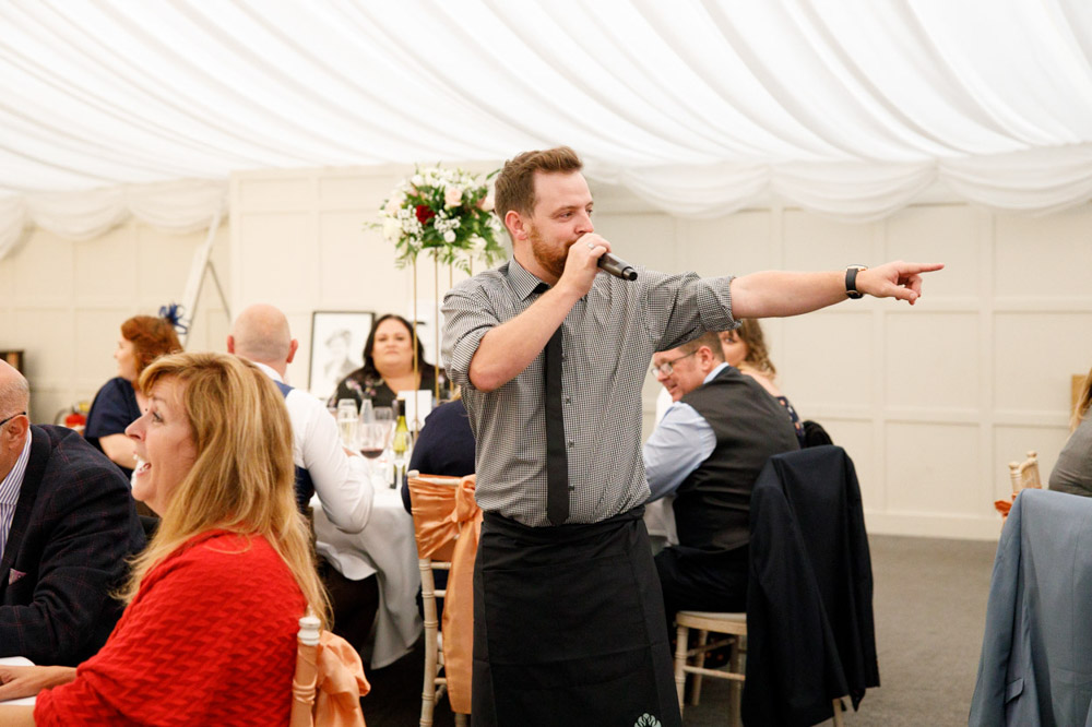 Singing waiter points to a dancing guest with flair.