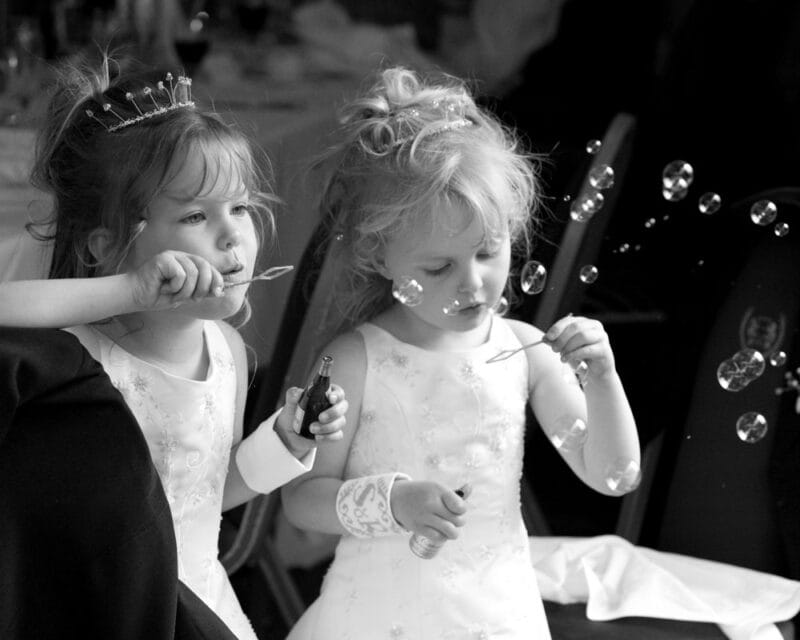 Two bridesmaids blowing bubbles at the wedding breakfast in black and white.