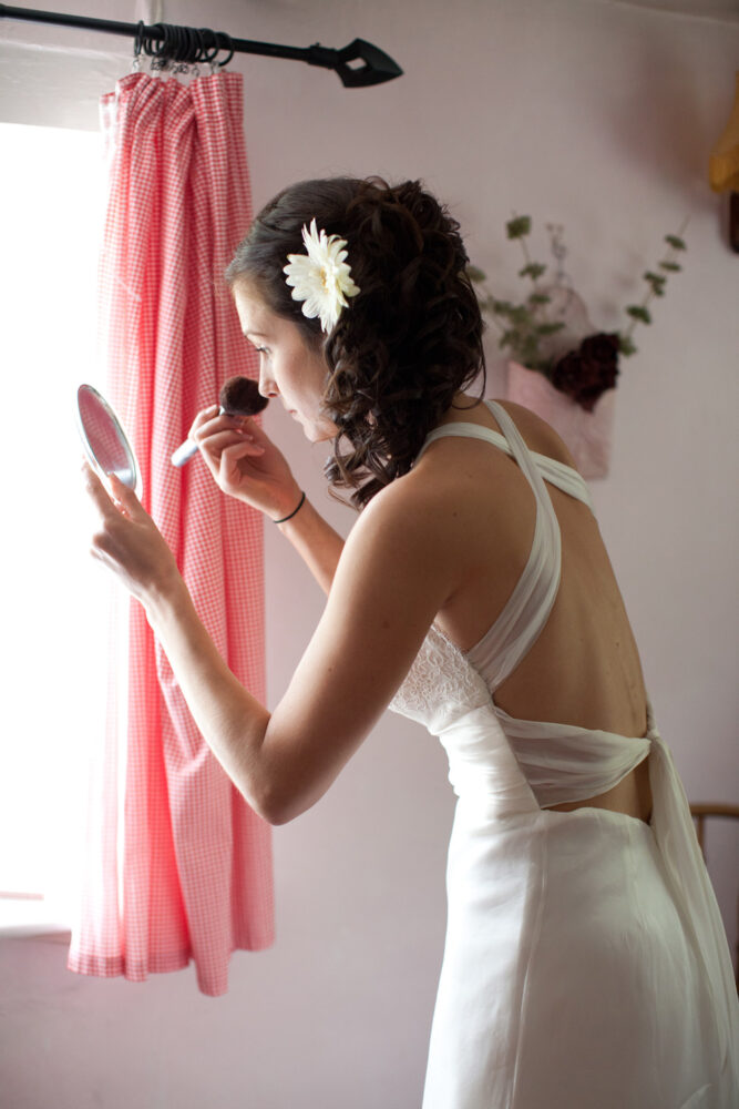 Bride with flower in her hair does final make up powdering her face holding a small mirror - unobtrusive wedding photography across Leeds and Yorkshire