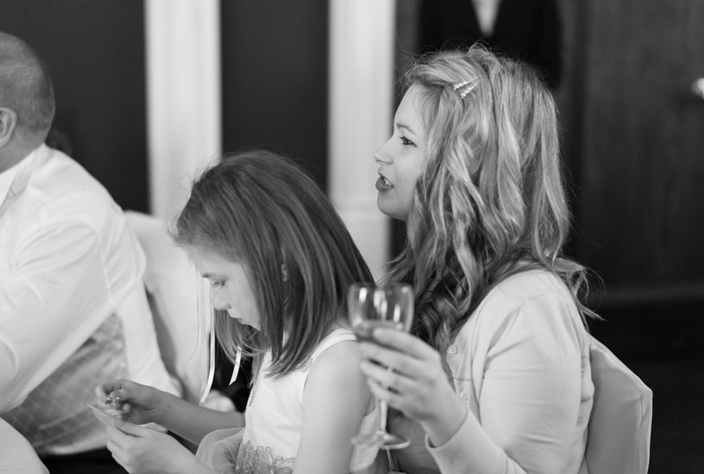 The groom’s sister bites her lip, laughing at the speech