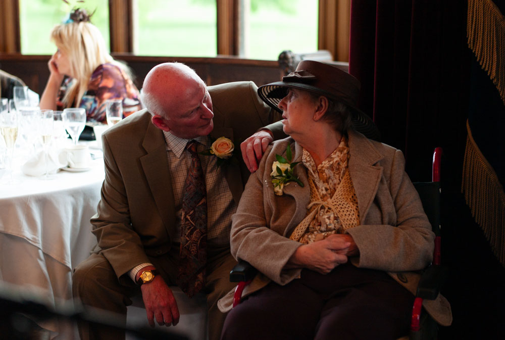 Smartly dressed great-grandparents sit side by side, sharing a quiet moment