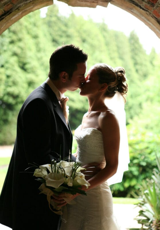 Close-up of bride and groom kissing with calla lilies bouquet in soft green tones
