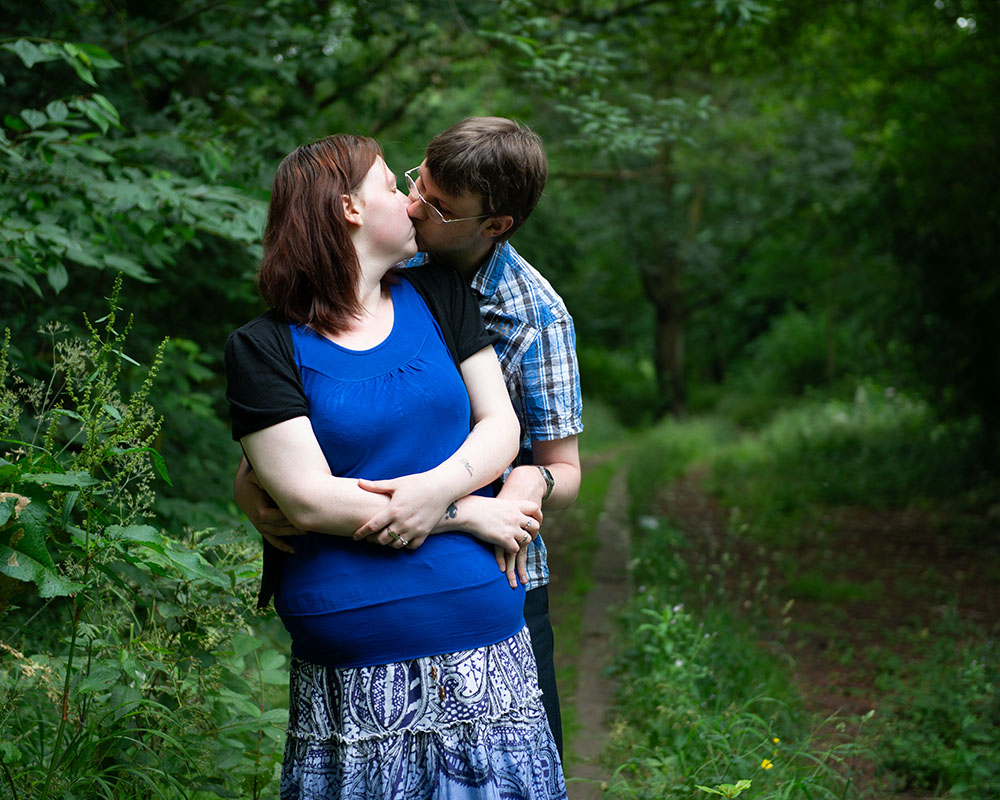 Rachel and Robert sharing a kiss with deep greenery behind, near the old model train path.