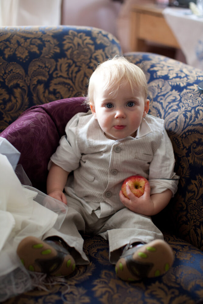 Little pageboy sat on the sofa with his apple in hand, caught in a candid moment.