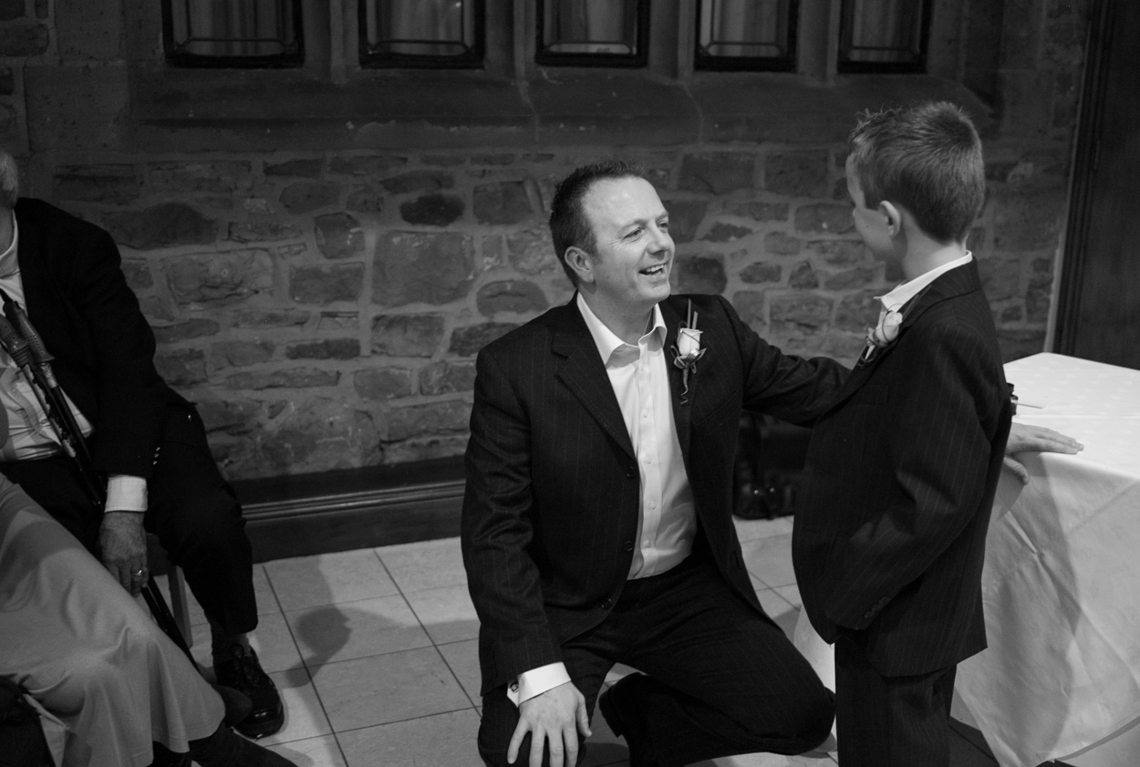 Groom crouched talking to his son the ring bearer in monochrome