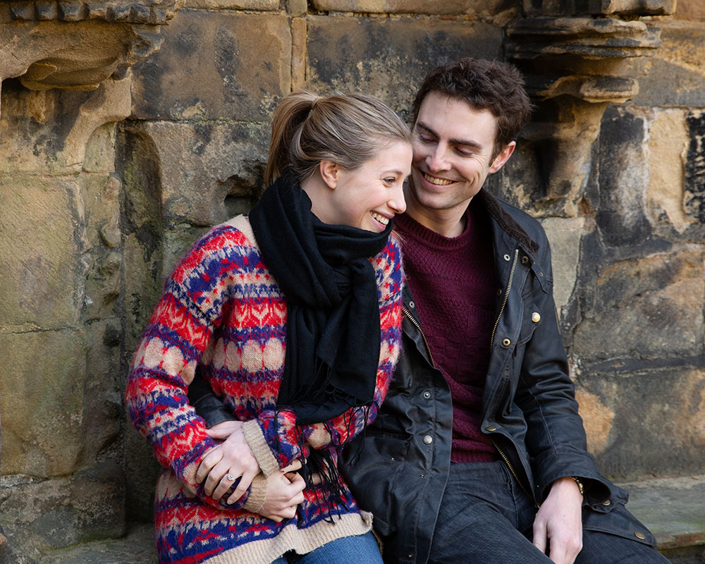 Zoe and Andrew smiling as the moment sinks in, standing within the ancient arches of Kirkstall Abbey.