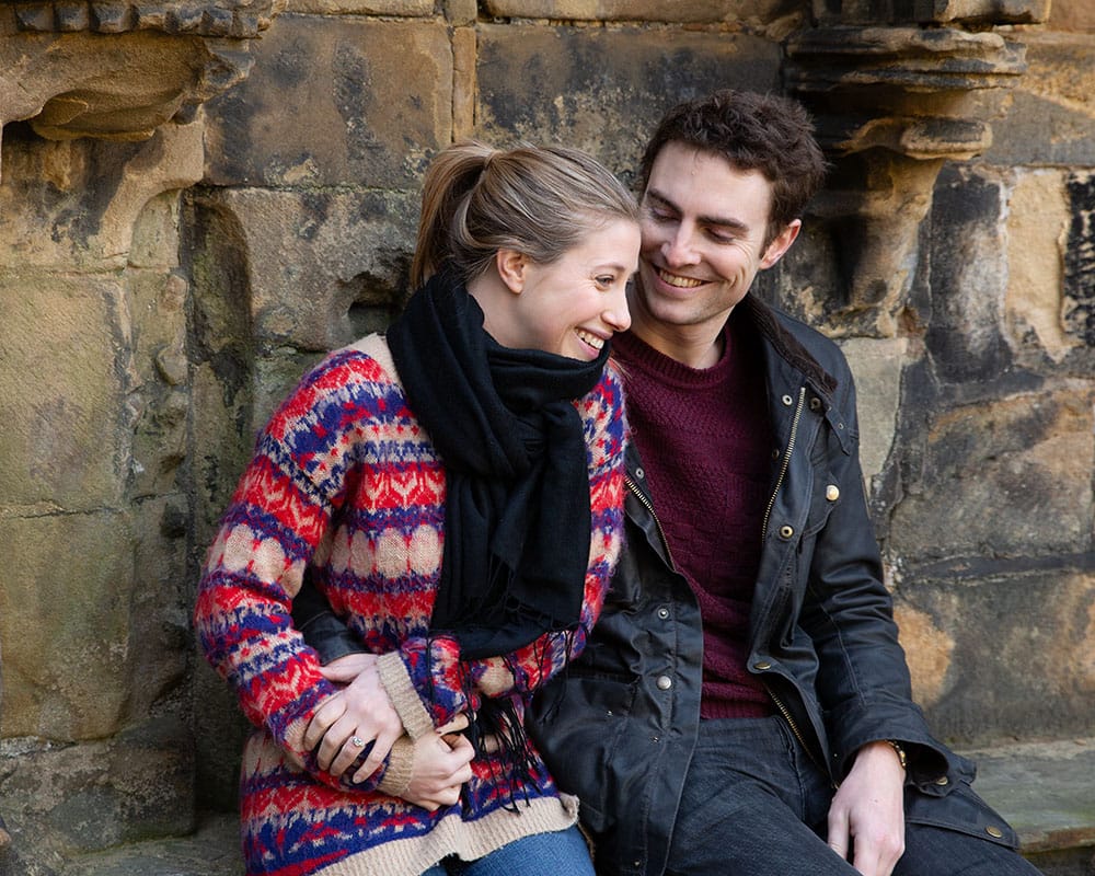 Zoe and Andrew smiling as the moment sinks in, standing within the ancient arches of Kirkstall Abbey.