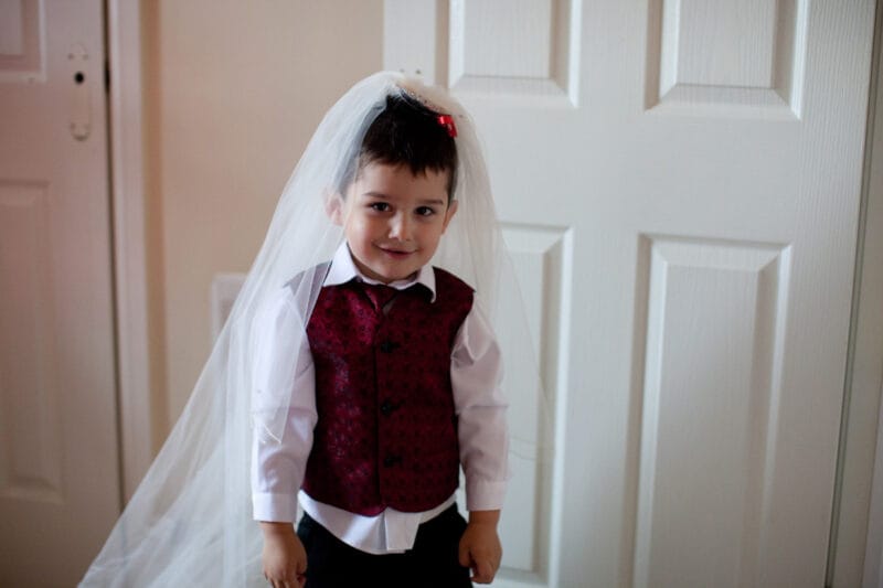 Bride’s little son smiling sweetly while wearing her veil — a playful moment.