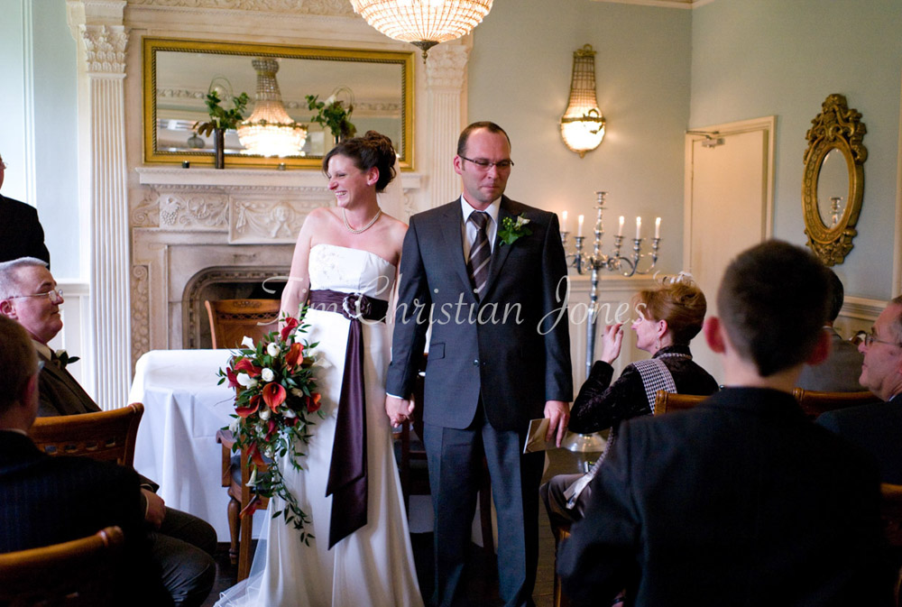 Julie and Pat leave the ceremony with relaxed smiles, bouquet swinging at her side.