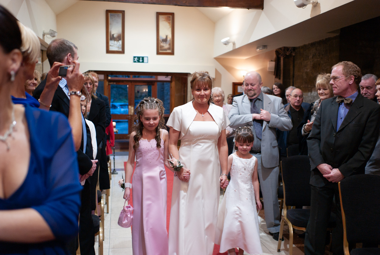 Bride enters with her daughters, smiling at her groom