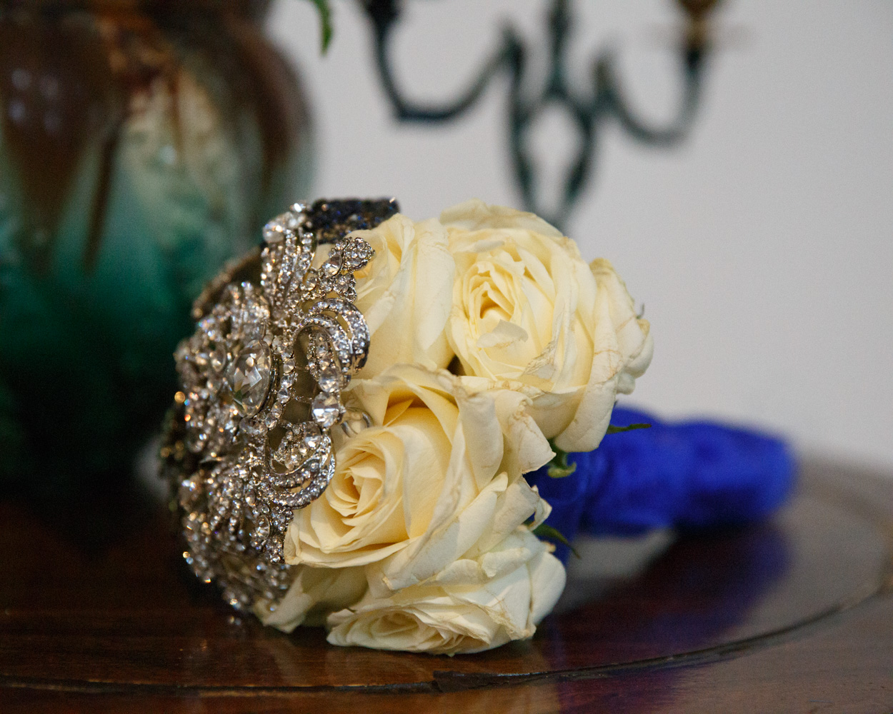 A bouquet of cream roses with silver details and blue-purple ribbon rests on a table