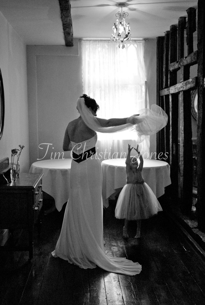 Julie lifts her veil playfully as her young daughter jumps up, reaching with delight.