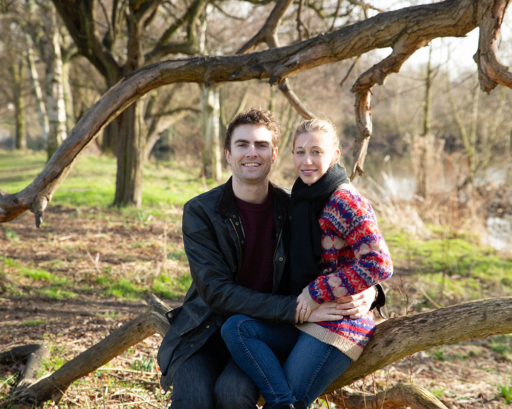Wrapped warm in scarves, Zoe and Andrew sit on a tree branch with Kirkstall greenery behind them.