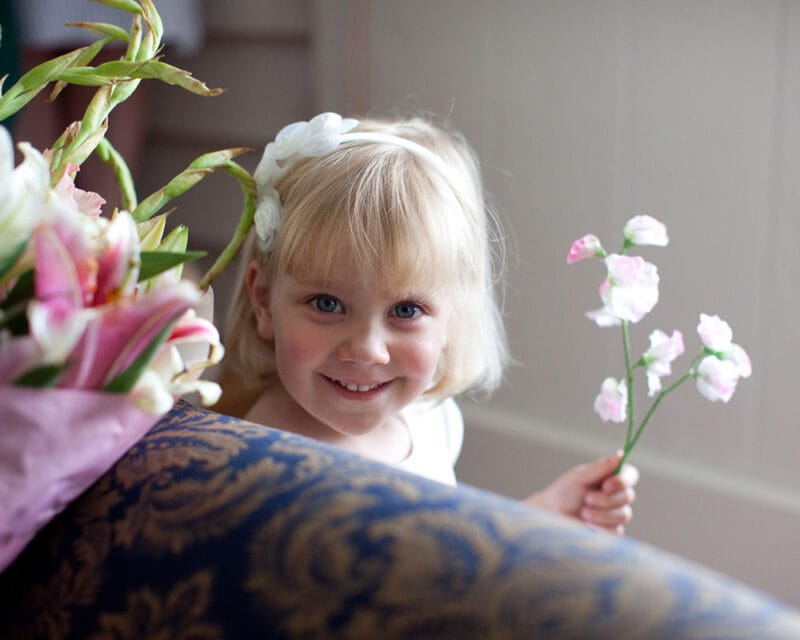 Bridesmaid smiling as she peeks from the sofa, flowers in hand.
