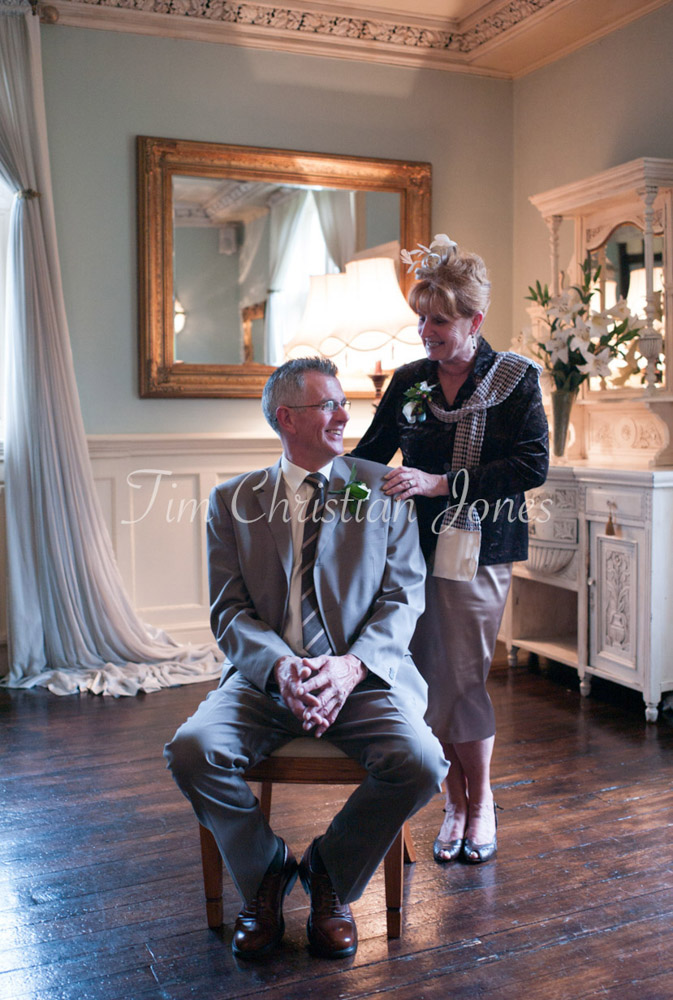 A gentle portrait of the bride’s parents — one seated, one standing — quietly composed.