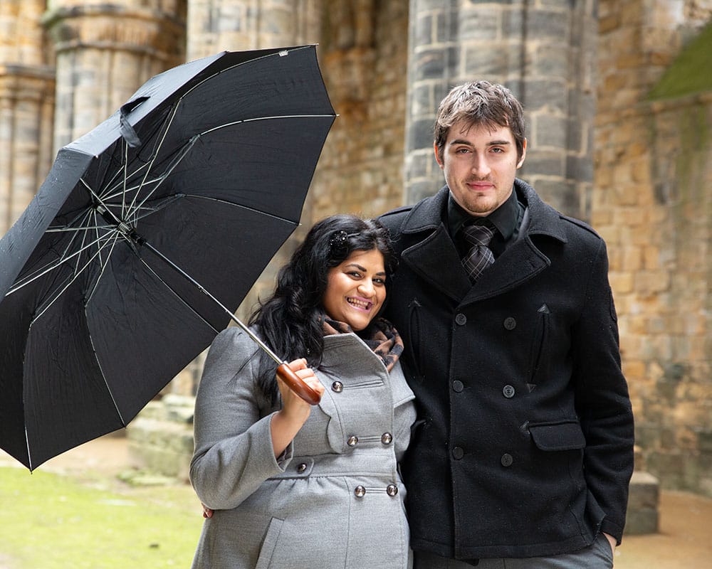 Zehra and Richard smiling inside Kirkstall Abbey, Zehra playfully holding up an umbrella with no rain in sight.