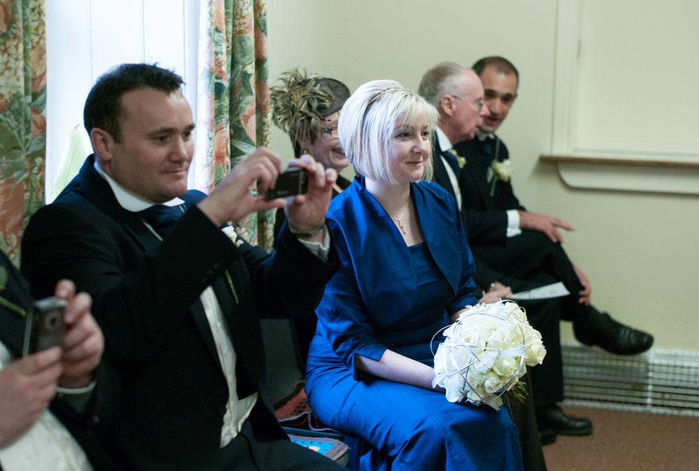 A smiling bridesmaid in mid-blue looks towards the couple.