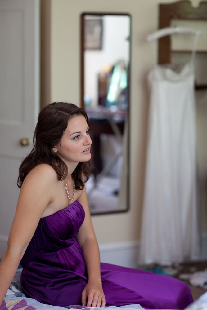 The bride natural photo sat on the bed with the bride's dress in the background by Yorkshire wedding photographer