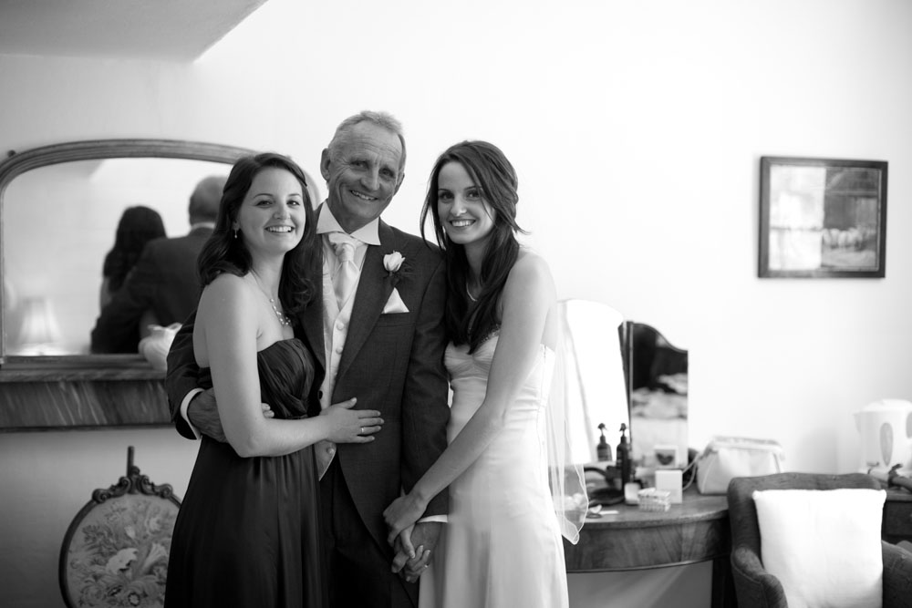 A lovely B&W photo with 3 looking into the camera - the bride, father, and bridesmaid