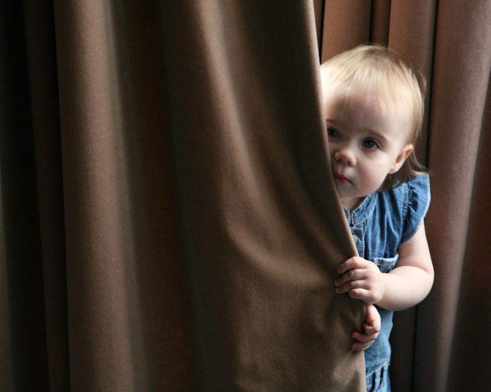 Little one shy peeping from behind the curtain