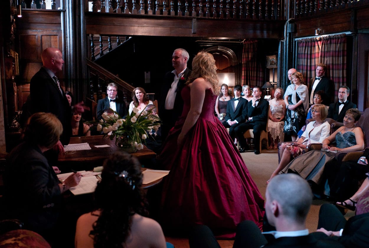 The couple standing at the ceremony table with guests seated all around in the cosy Mitton Hall room.