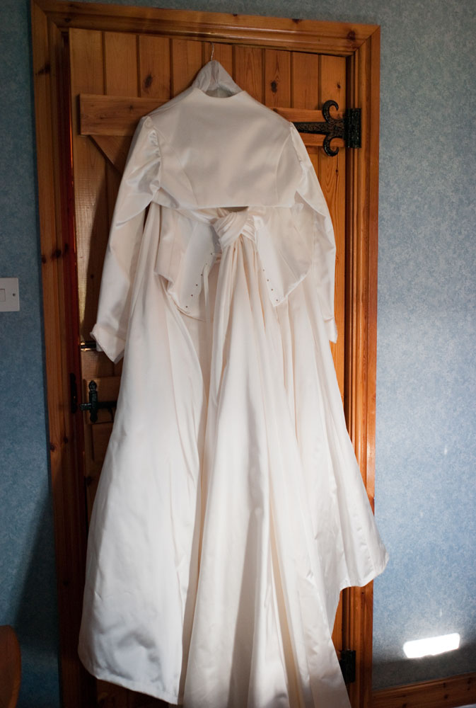 At Simonstone Hall Hotel - A February wedding moment - the bride's dress a heavy satin masterpiece hung on the wooden door in the bridal suite