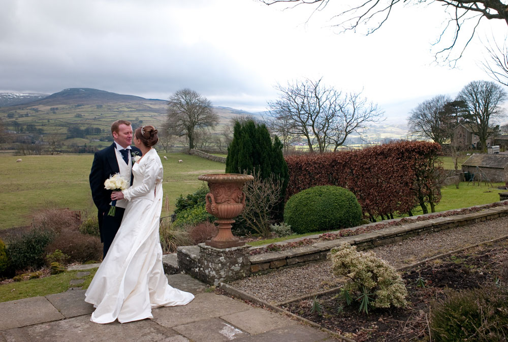 The couple close together with the gardens, hills, and grey clouds of North Yorkshire behind.