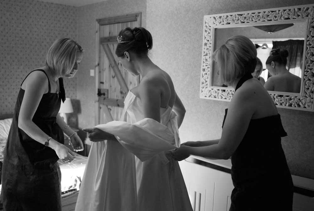 Bridesmaids helping fasten the brides satin dress in black and white - candid moments