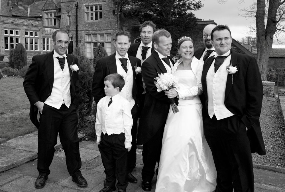 A black and white photo of the groom and groomsmen sharing a laugh with the bride.