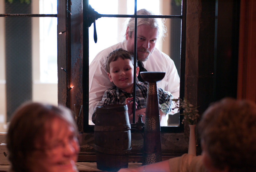 A little boy is lifted up to peek through a window at family inside.