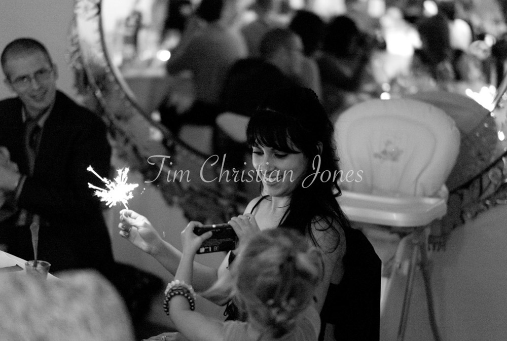 A group of guests laugh together, holding sparklers aloft as the room glows.