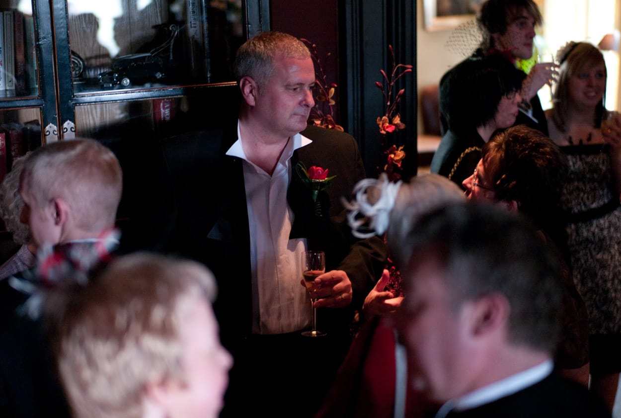 Groom standing with his bowtie untied, offering a casual look admired by a future couple.