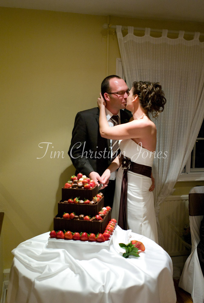 Julie and Pat kiss over the cake knife, hands together on the handle over soft white cloth.