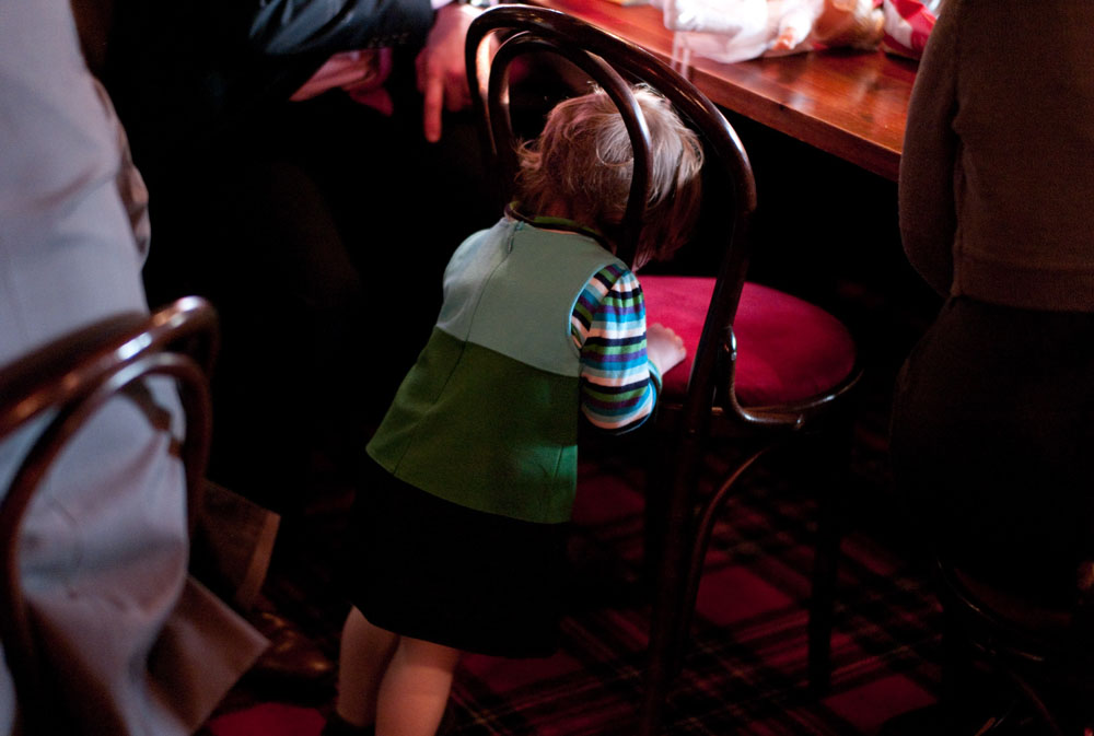A young child pokes her head through the back of a wooden chair, playfully.