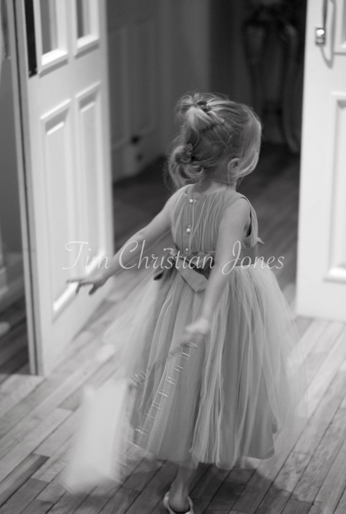 The little bridesmaid rushes joyfully through a doorway, dress swirling behind her.