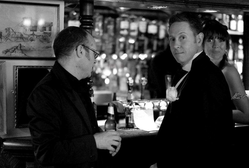 A groomsman notices the camera at the bar, raising an eyebrow mid-pour.