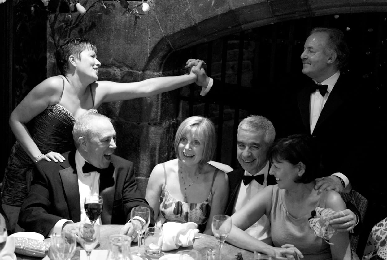 Monochrome photo of guests joining hands across a table in affection.