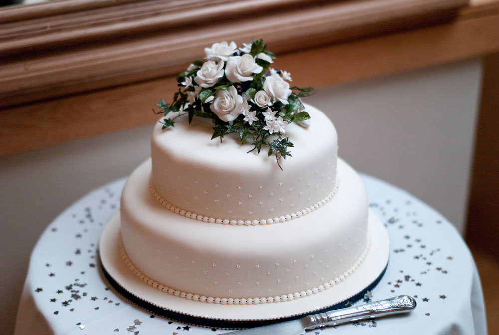 A close-up of the simple two-tiered wedding cake topped with roses.