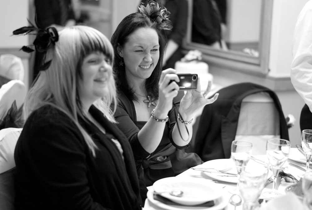 Female guests sit smiling, phones in hand, capturing the moment.