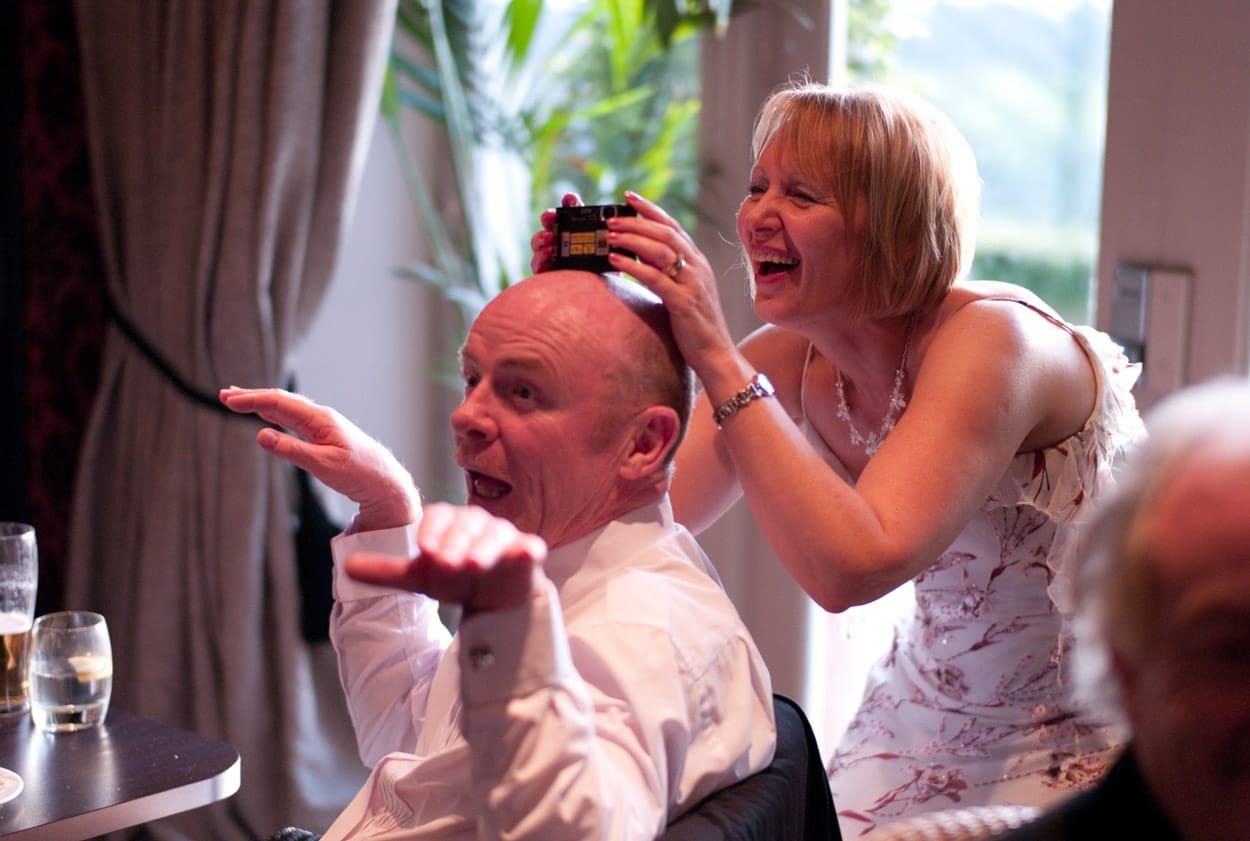 Female guest using her husband as a camera rest in a playful moment.