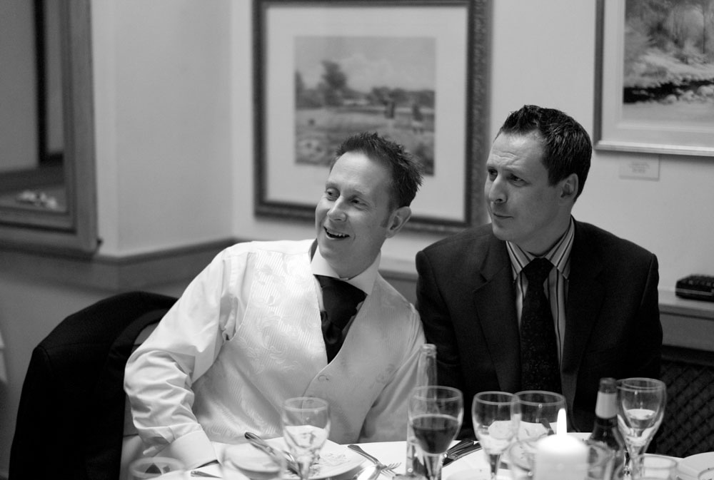 Two male guests pose with exaggerated smiles at a nearby table.