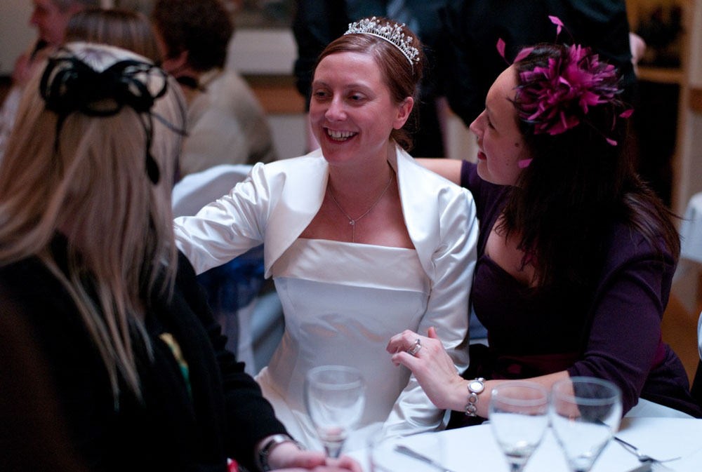 The bride sits between friends, mid-conversation and surrounded by joy.