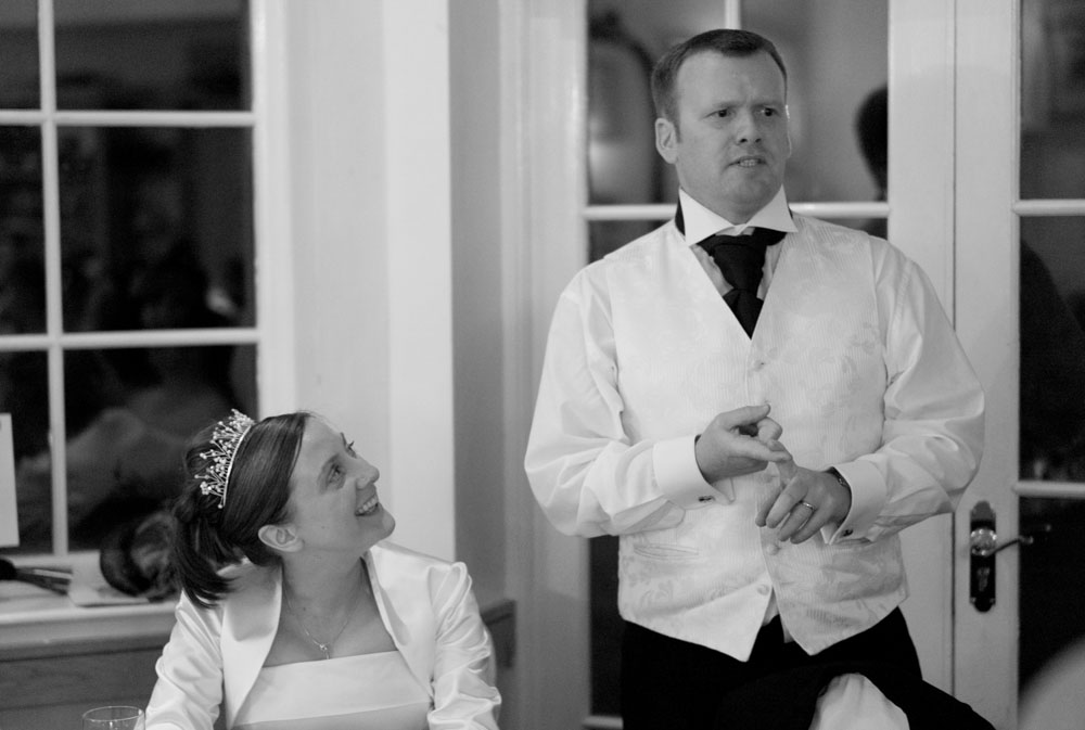 The groom begins his speech while his bride smiles back at him.