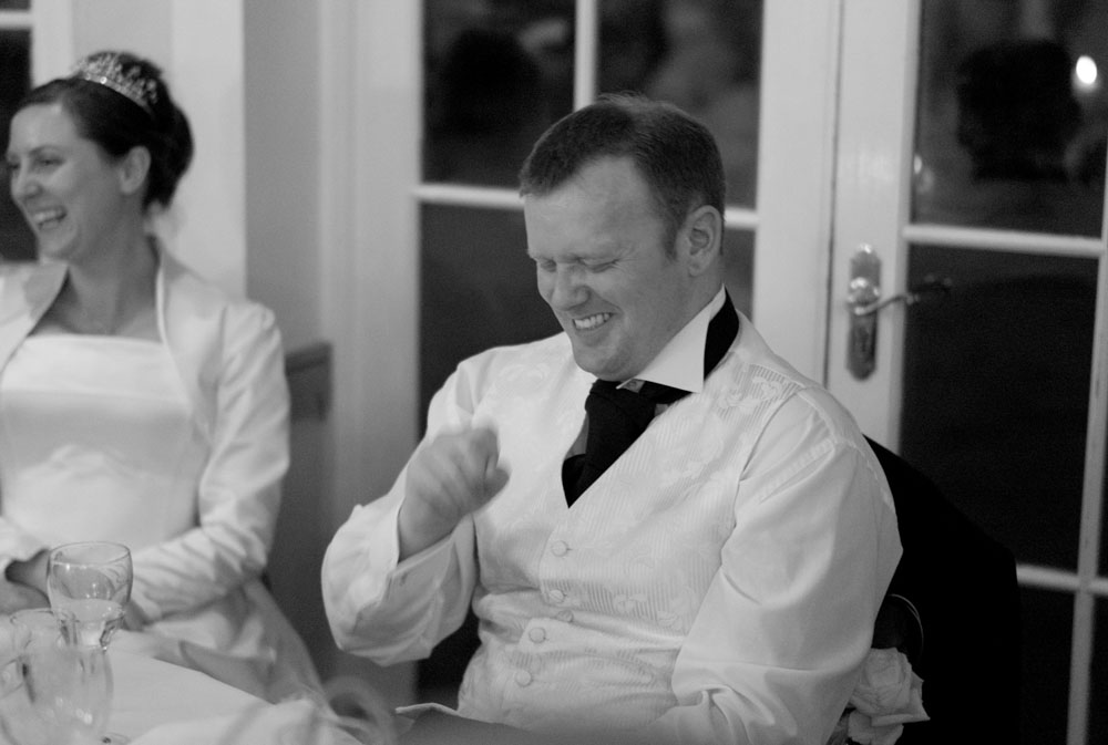The groom laughs with a mix of pride and slight embarrassment during the speeches.