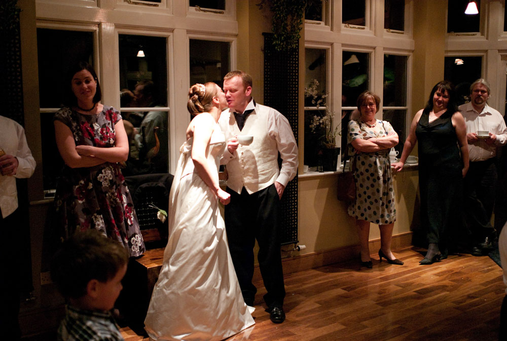 The bride leans in to kiss the groom as he holds his coffee.