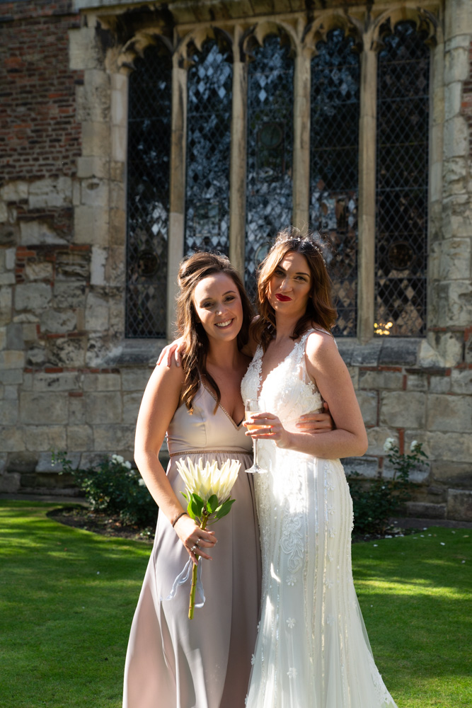 Bride and bridesmaid sharing a hug in dappled sunlight at Merchant Adventurers’ Hall in York, captured naturally by a Leeds wedding photographer