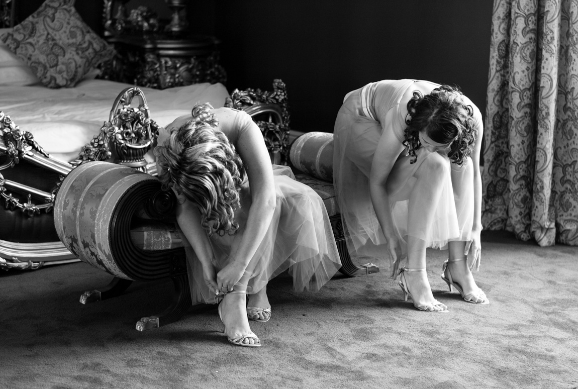Bridesmaids fastening their shoes while seated on a chaise in the bridal suite at Allerton Castle
