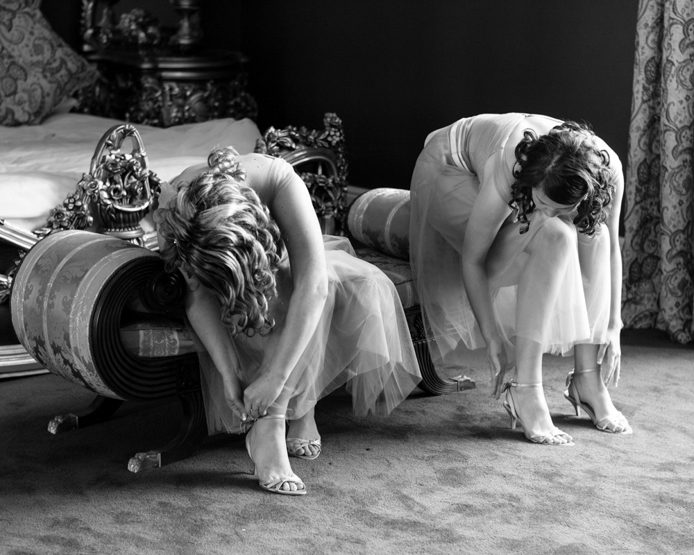 Allerton Castle wedding by Tim Christian Jones - Bridesmaids sat on a chaise at the foot of the bed in the bridal suite - fastening their shoes in monochome.